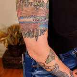 "Close-up of a colorful forearm tattoo with cityscape and nature elements, shown on moisturized skin to highlight brightness and ink clarity. Ideal for showcasing tattoo aftercare results using Kiwi Glow Tattoo Oil."