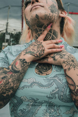 A heavily tattooed person highlighting healed neck and arm tattoos, showing crisp linework and detailed blackwork.