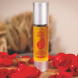 Kiwi Glow's Rosie Face Oil sits in a brown space on wood with red roses in the foreground. The bottle is yellow and has the Kiwi Glow Leaf Logo on the center area of the bottle. It reads: "Kiwi Glow... Face Oil Moisterizer... Rosie...net 1.7 fl oz."